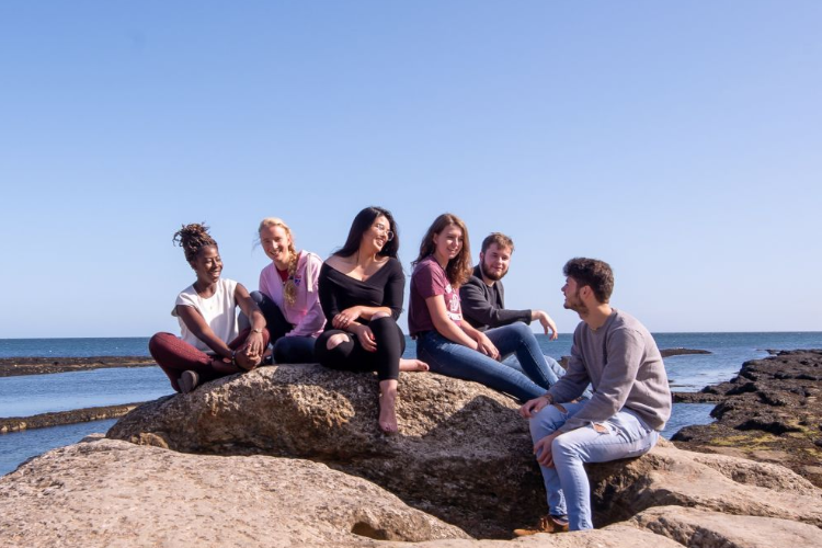 Students sitting on a rock near the beach